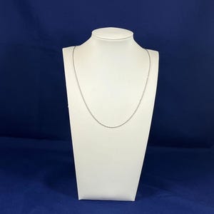May include: A silver chain necklace on a white display stand. The chain is thin and delicate.