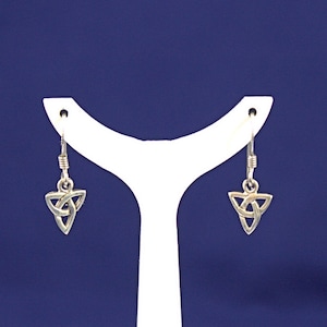 May include: A pair of silver-toned Celtic knot earrings. Each earring features a triangular knot design suspended from a simple hook. The earrings are displayed against a blue background on a white earring stand.