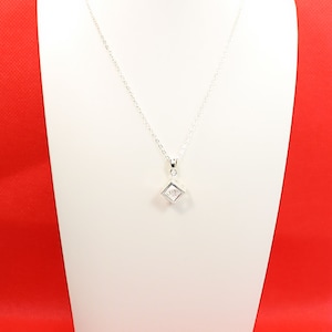 May include: A silver chain necklace with a square pendant featuring a clear crystal in the center.