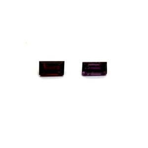 May include: Two rectangular gemstones with a deep red and purple hue. The gems are set against a white background, showcasing their color and cut. Ideal for jewelry making or collecting.