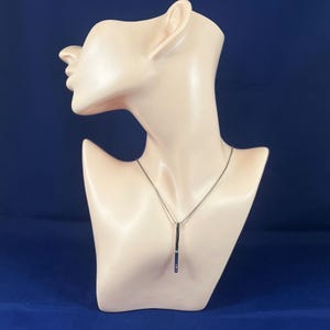 May include: A silver necklace with a long, thin pendant. The pendant has a vertical line design with small, clear stones.