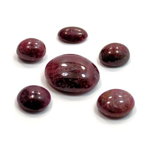 May include: Six cabochon cut gemstones, all a deep reddish-purple colour. The stones are oval and round in shape, and they have a smooth, polished finish.