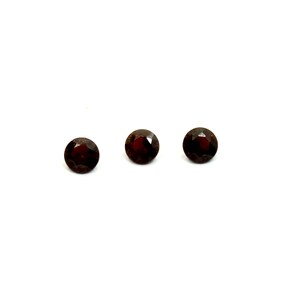 Peut inclure: Trois pierres précieuses rondes de couleur rouge foncé sur un fond blanc.