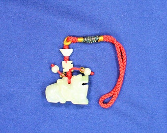 May include: A jade green carved frog charm with a red string and gold accents. The frog is sitting on a blue surface.