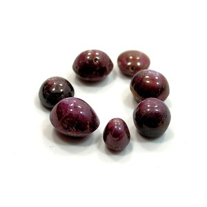 Peut inclure: Un ensemble de perles de pierres précieuses polies, rouge foncé, disposées en cercle. Les perles varient en taille et en forme, avec une surface brillante et des inclusions visibles. Idéal pour la création de bijoux.