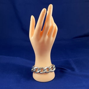 May include: A silver curb chain bracelet with large links. The bracelet is on a mannequin hand.