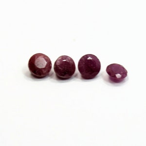 May include: Four oval-shaped gemstones, with a reddish-purple hue, are arranged in a row on a white surface.