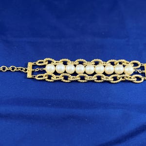 May include: A gold chain bracelet with a row of white pearls. The bracelet has a lobster clasp closure.