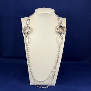 May include: A silver chain necklace with two large, interlocking circular links. The necklace is layered with a smaller chain.