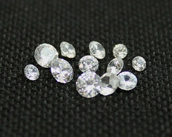 May include: A group of clear, faceted gemstones, likely diamonds, scattered on a black fabric background.
