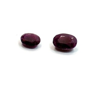 May include: Two oval-shaped gemstones, both a deep purple colour. The gemstones are smooth and polished.