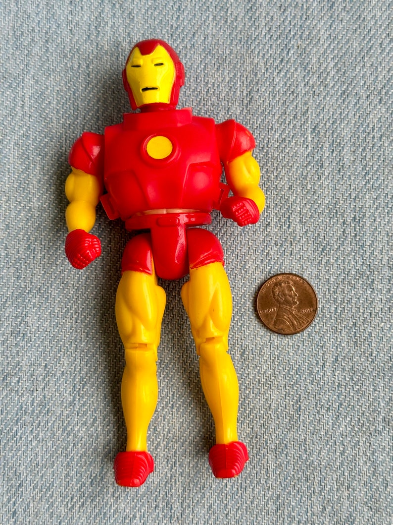 Może przedstawiać: Plastikowa figurka Iron Mana w kolorze czerwonym i ż&oacute;łtym. Figurka stoi na niebieskim dżinsowym tle.