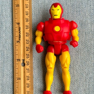 Może przedstawiać: Plastikowa figurka Iron Mana w kolorze czerwonym i ż&oacute;łtym. Figurka ma około 10 cm wysokości i szczeg&oacute;łową twarz z ż&oacute;łtym hełmem i czerwonymi oczami. Figurka jest ustawiona z rękami po bokach i lekko rozstawionymi nogami.