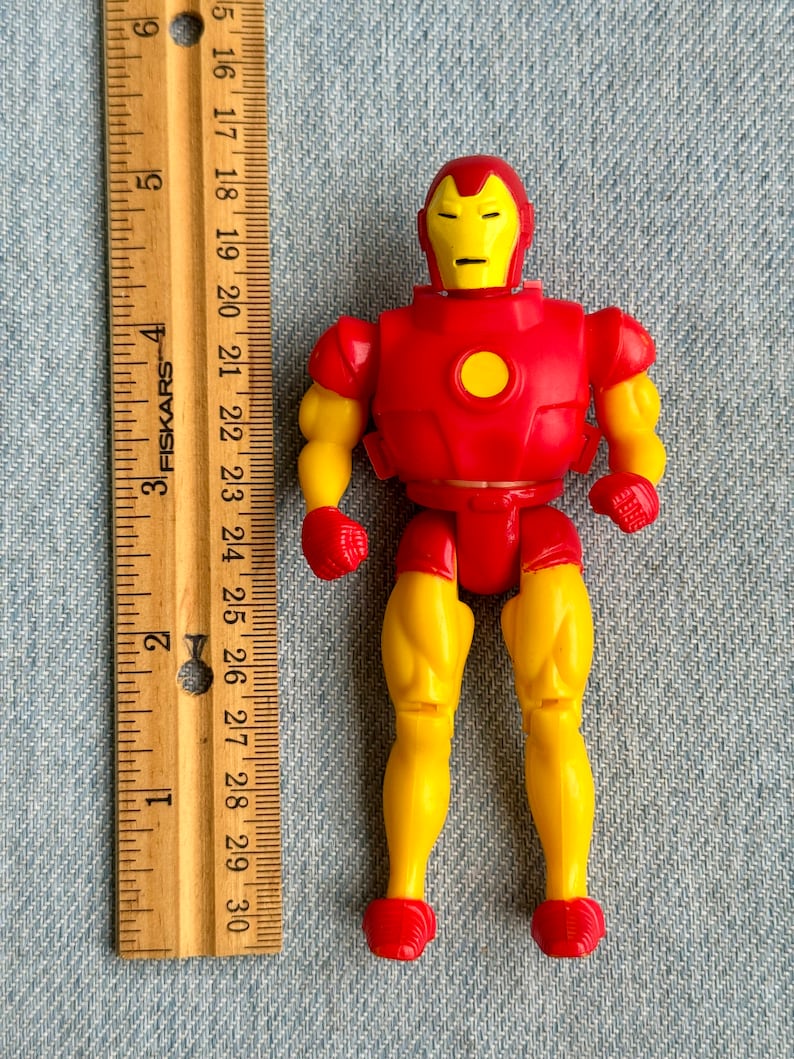 Może przedstawiać: Plastikowa figurka Iron Mana w kolorze czerwonym i ż&oacute;łtym. Figurka ma około 10 cm wysokości i szczeg&oacute;łową twarz z ż&oacute;łtym hełmem i czerwonymi oczami. Figurka jest ustawiona z rękami po bokach i lekko rozstawionymi nogami.