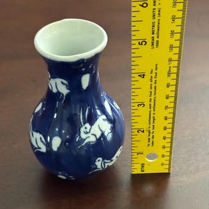 May include: A small blue and white ceramic vase with a design of white rabbits on a blue background. The vase is approximately 5 inches tall.
