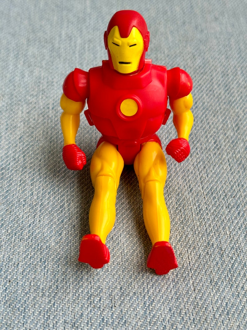 Może przedstawiać: Plastikowa figurka Iron Mana, superbohatera z komiks&oacute;w Marvela, w kolorze czerwonym i ż&oacute;łtym. Figurka siedzi ze skrzyżowanymi nogami i zgiętymi ramionami.