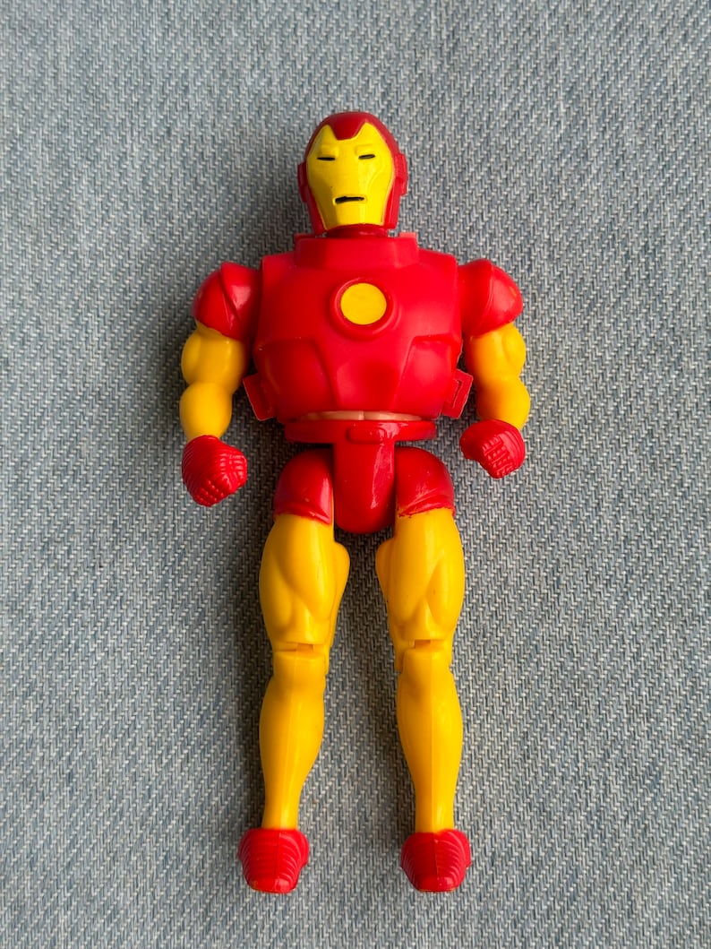 Może przedstawiać: Plastikowa figurka Iron Mana w kolorze czerwonym i ż&oacute;łtym. Figurka ma ż&oacute;łtą twarz z czerwoną maską i czerwoną płytę piersiową z ż&oacute;łtym kołem w środku.