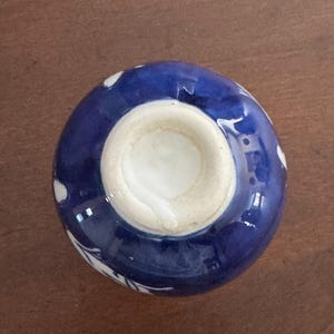 May include: A small, blue and white ceramic bowl with a floral design. The bowl is turned upside down, revealing a white glazed interior.