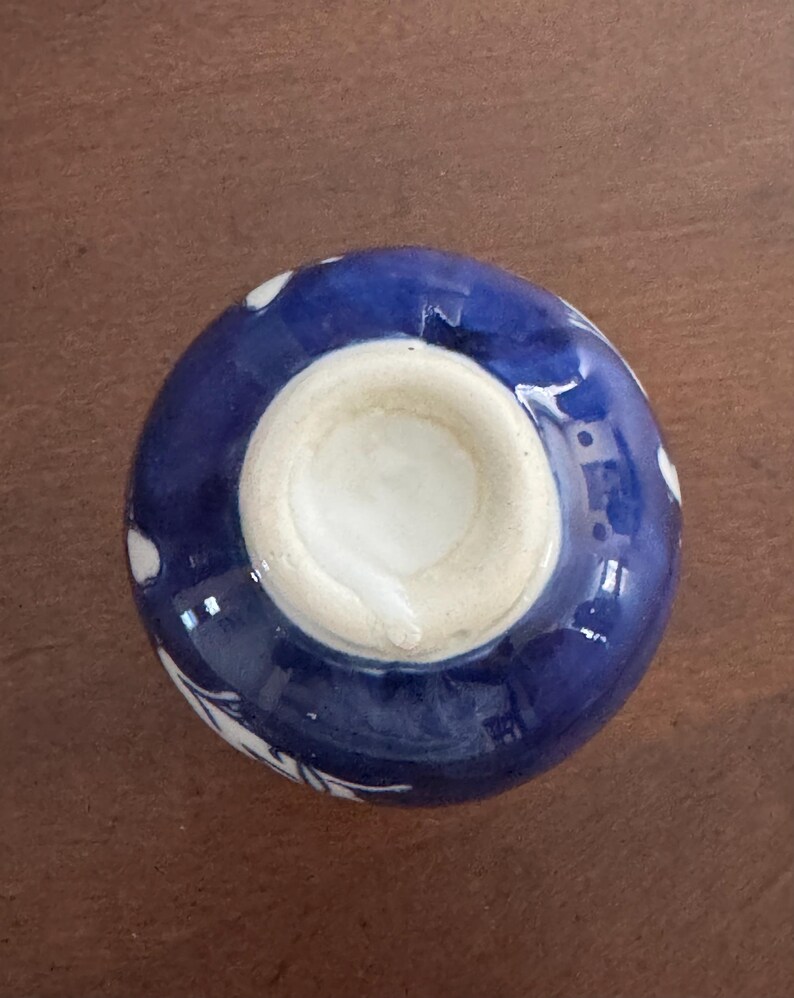 May include: A small, blue and white ceramic bowl with a floral design. The bowl is turned upside down, revealing a white glazed interior.