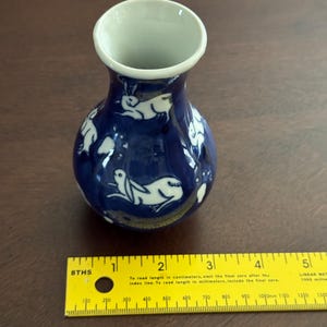 May include: A small blue and white ceramic vase with a white rabbit design. The vase is about 4 inches tall.