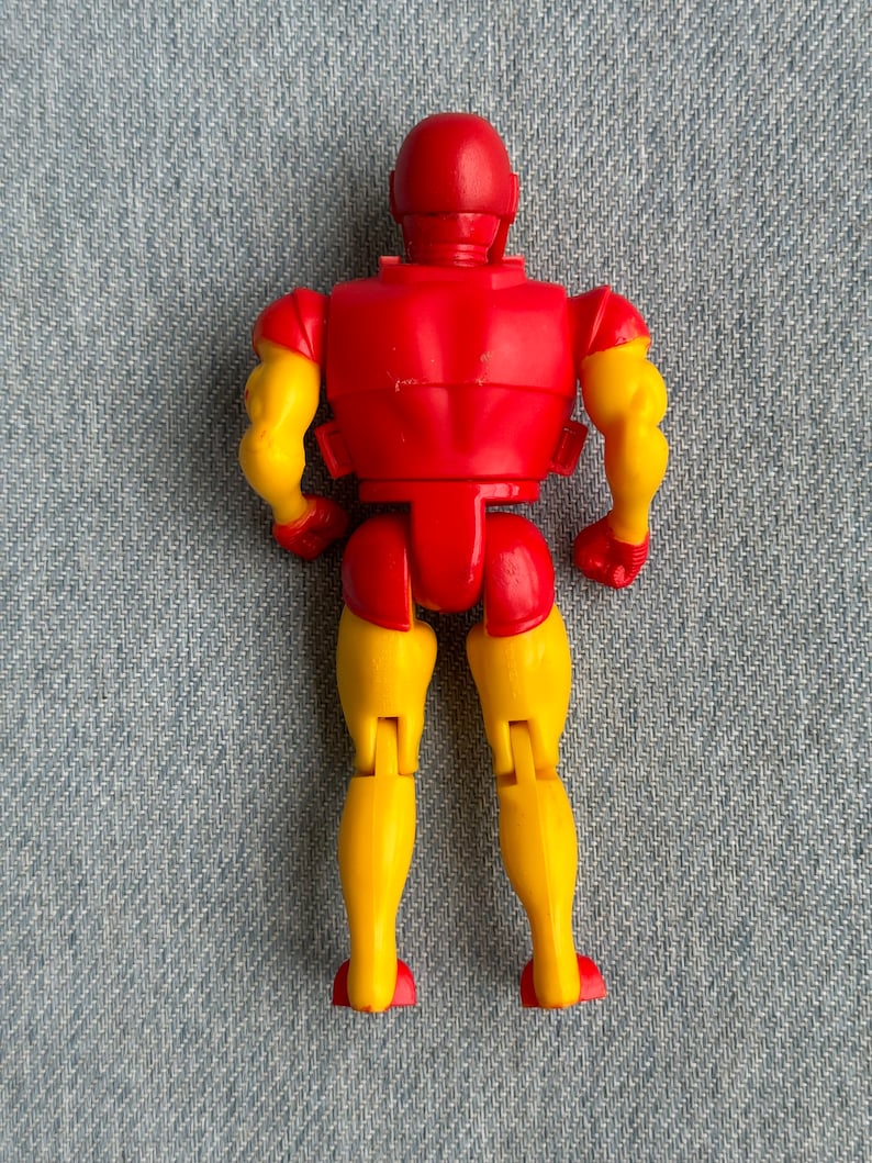 Może przedstawiać: Plastikowa figurka Iron Mana w kolorze czerwonym i ż&oacute;łtym, stojąca tyłem do kamery. Figurka ma czerwony tuł&oacute;w i głowę, ż&oacute;łte ramiona i nogi oraz czerwony hełm.