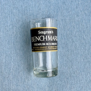 May include: A clear glass with a black and gold label that reads "Seagram's Benchmark Premium Bourbon Kentucky Straight Bourbon Whiskey"