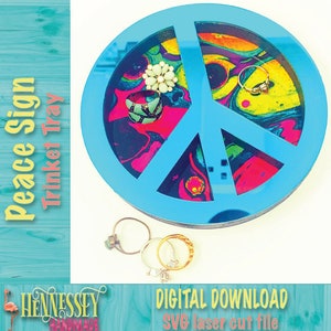 May include: A blue peace sign shaped trinket tray with a colorful abstract design. The tray is made of wood and has a cutout peace sign design. The tray is perfect for holding small items like jewelry or keys. The text "Peace Sign Trinket Tray" is written vertically on the left side of the image. The text "DIGITAL DOWNLOAD SVG laser cut file" is written on the bottom right side of the image.