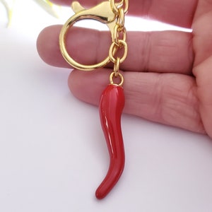 May include: Gold keyring with a red chilli pepper charm. The keyring has a lobster clasp and a circular ring.