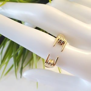 May include: Gold ring featuring two hands making the 'rock on' hand gesture.