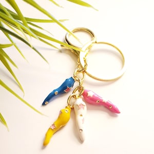 May include: A gold key chain with four colourful chili pepper charms. The charms are blue, yellow, white, and pink with pink stars on each.