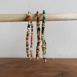 May include: Three beaded bracelets with gold accents. The bracelets are made with colorful beads in shades of red, orange, yellow, green, blue, and black.