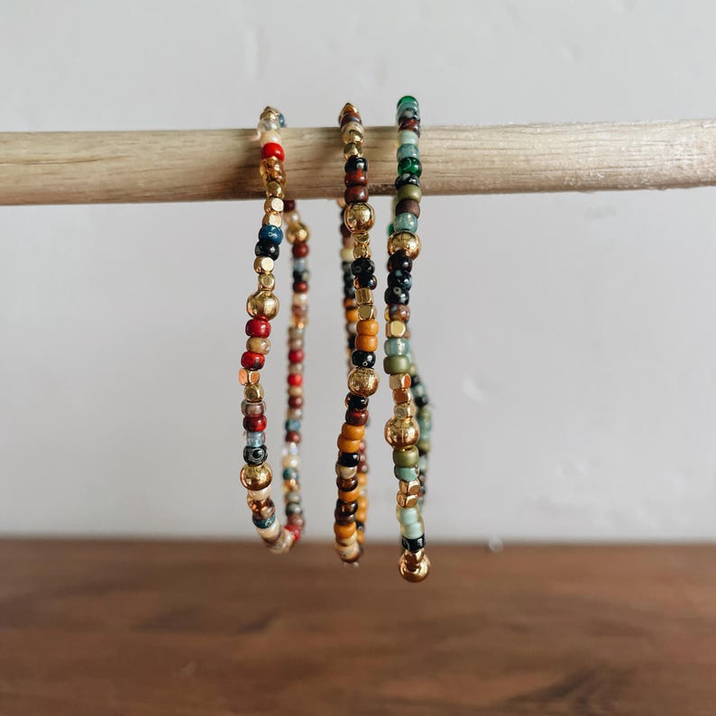 May include: Three beaded bracelets with gold accents. The bracelets are made with colorful beads in shades of red, orange, yellow, green, blue, and black.