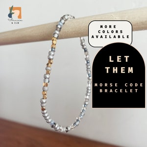 May include: A silver and gold beaded bracelet with the words "Let Them" and "Morse Code Bracelet" on a black and white background.
