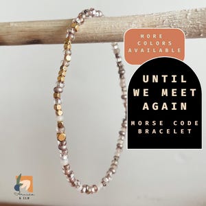 May include: A delicate gold and white beaded bracelet with the message "Until We Meet Again" in Morse code. The bracelet is displayed on a wooden surface.