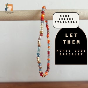 May include: A colorful beaded bracelet with gold accents. The bracelet is made of small, round beads in shades of red, orange, blue, and gray. The text "LET THEM" and "MORSE CODE BRACELET" is printed on a black background.