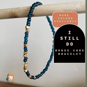 May include: A teal blue beaded bracelet with gold accents. The bracelet spells out "I Still Do" in Morse code. The text "More Colors Available" is in a peach colored circle. The text "I Still Do Morse Code Bracelet" is in a black circle.