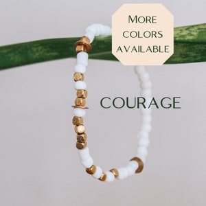 May include: White and gold beaded bracelet with the word "COURAGE" printed on it. More colors are available.