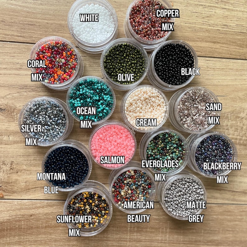 May include: Assortment of 14 small containers filled with various colors of seed beads. The containers are labeled with the bead color names, such as "Coral Mix", "Silver Mix", "Montana Blue", "Copper Mix", "White", "Black", "Olive", "Ocean Mix", "Cream", "Salmon", "Everglades Mix", "Sunflower Mix", "American Beauty", "Matte Grey", "Sand Mix", and "Blackberry Mix".