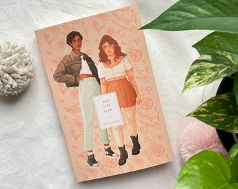 May include: A book cover with a peach background featuring two people standing next to each other. The book title is "One Last Stop" with the author's name "Casey McQuiston" below. The cover has a floral pattern with oranges, mushrooms, and cassette tapes.