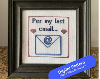 May include: Framed cross-stitch art featuring the text "Per my last email..." above a blue email envelope symbol. Two small heart shapes are on either side of the text. The frame is dark brown and the background is white.