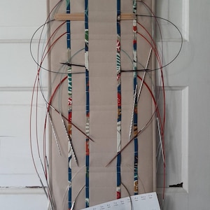 May include: A beige knitting needle organizer with a floral and paisley patterned top and bottom. The organizer holds various sizes of circular knitting needles, with the text "Wonderfully Made" visible.