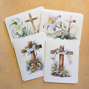 May include: Four cards with a white background and a brown wooden cross with white flowers and a white ribbon on each card. The crosses are surrounded by white flowers and green leaves.
