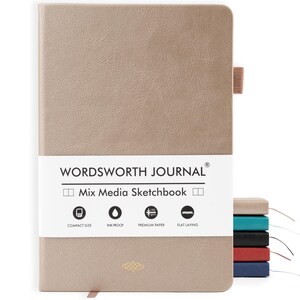 May include: A beige Wordsworth Journal Mix Media Sketchbook with a textured cover. The journal features a white band with the brand name and product details. Additional journals in various colors are stacked to the right.