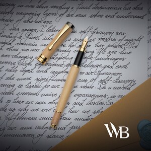Puede incluir: Una pluma estilogr&aacute;fica de madera con detalles dorados y un agarre negro, sobre una carta manuscrita. La tapa de la pluma est&aacute; quitada, revelando el plum&iacute;n. El fondo incluye escritura cursiva y un sello de cera.