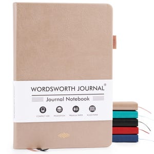 May include: A beige Wordsworth Journal notebook with a textured cover. The notebook features a white band with the text "WORDSWORTH JOURNAL" and icons indicating compact size, pagination, premium paper, and ruled paper. A stack of colorful notebooks is visible.