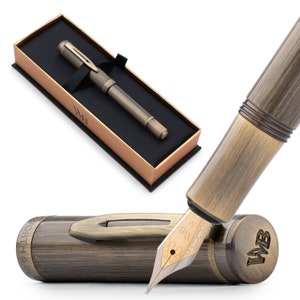 May include: A gold-toned fountain pen with a black ink cartridge and a gold-toned nib. The pen is in a box with the initials "WB" on the lid. The pen is also shown with the cap off, revealing the nib and the ink cartridge.