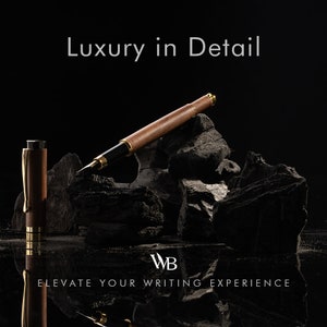 Op de afbeelding: Een bruine en gouden vulpen met een houten vat en gouden accenten ligt op een stapel zwarte houtskoolstenen. De tekst "Luxury in Detail" staat boven de pen, en de tekst "WB Elevate Your Writing Experience" staat onder de pen.