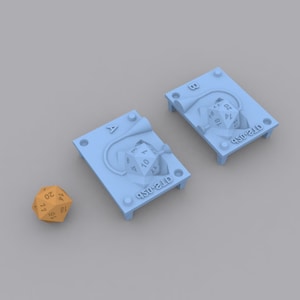 Puede incluir: Dos moldes de impresión 3D de color azul claro para hacer dados de 20 caras. Los moldes están etiquetados con "A" y "B" y tienen el texto "D20-STL" impreso en ellos. Un dado de 20 caras de color marrón está sentado sobre una superficie gris claro.