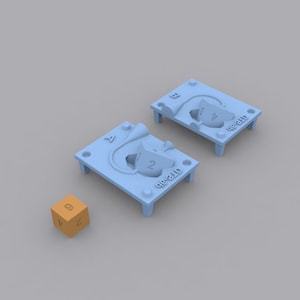 以下が含まれることがあります： 2つの薄い青色のプラスチック製のサイコロ型。それぞれに「D6-21D」という文字が書かれている。1つの型には「4」の面が上を向いたサイコロ、もう1つの型には「2」の面が上を向いたサイコロが入っている。手前に「4」の面が上を向いたオレンジ色のサイコロが1つある。
