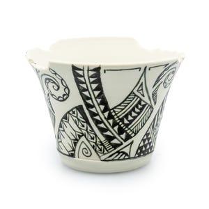 Può includere: Una ciotola in ceramica color crema con bordo svasato e motivo tribale nero. La ciotola presenta forme geometriche e linee, creando un design unico. Adatta per uso decorativo o funzionale. Il diametro della ciotola è di circa 15 cm.